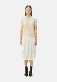 Beige stickad kortärmad tröja med texturerade horisontella ränder, kombinerad med en vit plisserad midikjol, avslutad med svarta ankelstövlar.