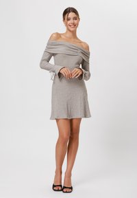 Grijze geribbelde off-shoulder jurk met lange klokvormige mouwen, een taille die cinched is en een uitlopende zoom. Van zacht, rekbaar breigaren.