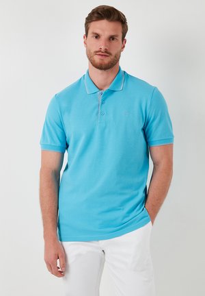 Camisa polo azul hecha de suave algodón, con mangas cortas, un cuello clásico y un logotipo sutil en el pecho. Textura suave, diseño ajustado.