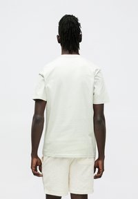 Light green cotton t-shirt with short sleeves and a classic crew neck, paired with patterned beige shorts, shown from the back.