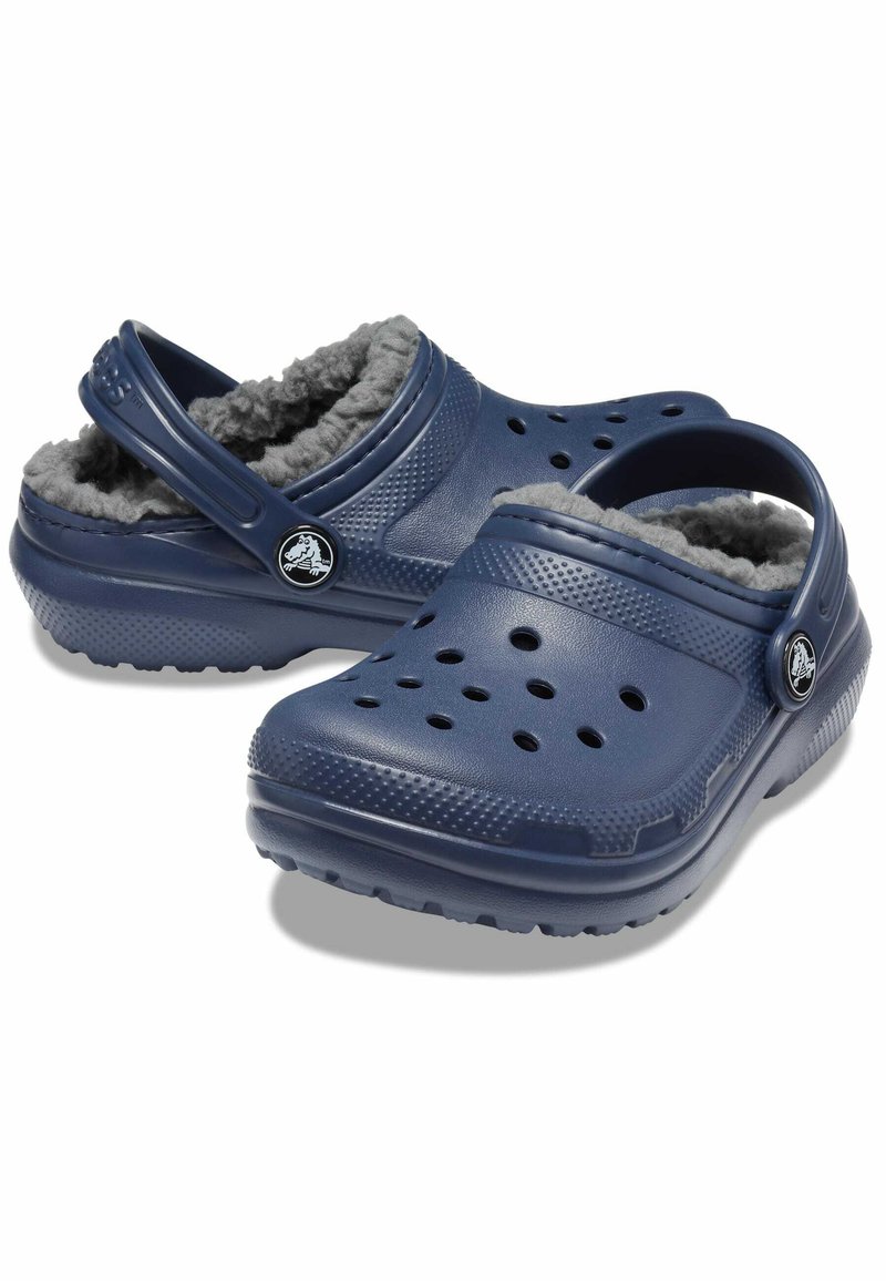 Marineblaue Clogs mit einer strukturierten, matten Kunststoffoberfläche. Fleece-Fütterung, Belüftungsperforationen und ein verstellbarer Fersenriemen.