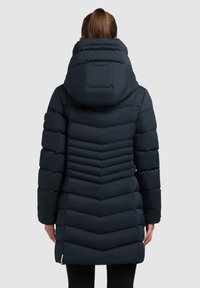 Mornarska puffer jakna s chevron šivom, velikim kapuco in z zadrgo na robu. Gladka tekstura, dolžina do sredine stegna.