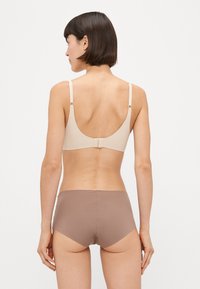 Beige sømløs bh med justerbare stropper og krok-lukking, kombinert med brune sømløse truser med middels høyde. Glatt stofftekstur.