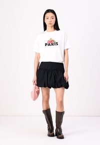 T-shirt blanc avec un graphisme "PARIS" et un design floral, associé à une jupe noire à volants, des bottes marron montantes et une pochette rose.