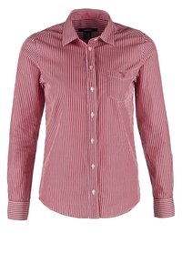 Chemise à rayures verticales rouges et blanches, manches longues, boutonnée, avec poche poitrine et col pointu.