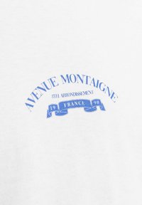 Balta medvilninė marškinėlių su mėlynu tekstu. Dizainas apima "AVENUE MONTAIGNE", "8-asis ARONDISSEMENTAS", "PRANCŪZIJA" ir juostelės grafiką.