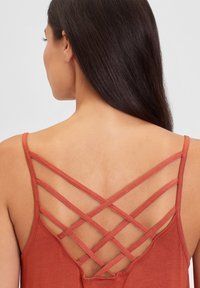 Top in colore ruggine con un design di spalline incrociate sul retro. Tessuto morbido con una vestibilità rilassata e una texture minima.