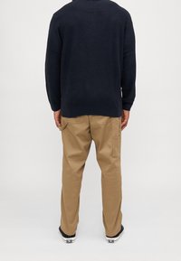 Marinblå stickad tröja med långa ärmar, kombinerad med khakifärgade cargobyxor med sidofickor. Tillgängliga skor är svarta sneakers.