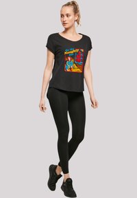 Black T-shirt with a graphic print featuring the text "On the Naughty List." Paired with black leggings and black sneakers.