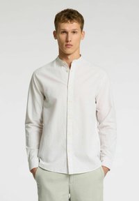 Camisa blanca de manga larga y con botones, con cuello mao, que presenta finas rayas verticales. La tela parece suave con un ligero brillo.