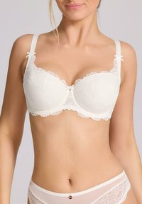 Biały koronkowy stanik z fiszbinami, ozdobiony kwiecistym wzorem, z usztywnianymi miseczkami, regulowanymi ramiączkami i małymi kokardkami na ramiączkach.