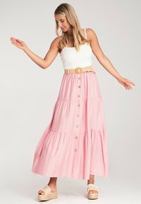 Hellrosa Maxikleid mit gestuften Design, Knöpfen vorne und einem geflochtenen Gürtel. Kombiniert mit beigen Plateausandalen.