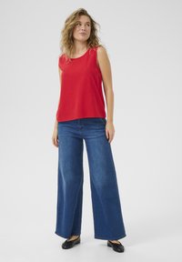 Punane särk ilma varrukateta, kombineeritud laia jalaga siniste denimsärkidega. Särgil on sile tekstuur, samas kui teksad omavad klassikalist denimfinišit. Mustad lamedad kingad täiendavad välimust.
