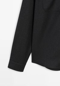 Schwarze Hemdmanschette aus strukturierter Stoff. Verfügt am Ende über eine Manschette und ein aufgenähtes Taschen-Detail am Körper. Einfaches Design.