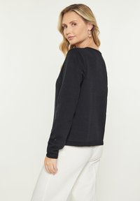 Pulover negru cu maneci lungi, guler rotund, de grosime medie, cu tiv și mansete ribbrate. Textură netedă, croi ajustat și detalii de design minime.