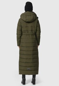 Lange, olijfgroene gewatteerde jas met een capuchon, een ceintuur in de taille en een horizontaal gewatteerd patroon. Gecombineerd met een zwarte muts en knie hoge laarzen.