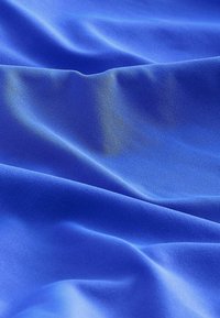 Blauwe stof met een gladde, zachte textuur, met zachte plooien en een lichte glans. De kleur is uniform felblauw zonder patronen.