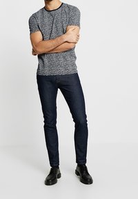 Košile s krátkým rukávem v námořnickém vzoru s kulatým výstřihem, nošená s tmavými slim-fit džíny a černými šněrovacími botami.