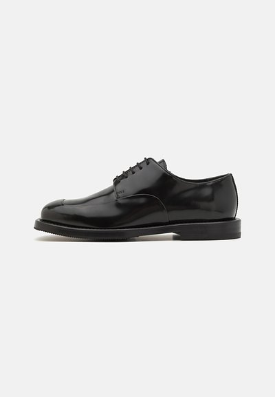 Chaussures habillées en cuir noir avec une finition brillante, bout rond, design à lacets, semelle contrastée et détails de coutures minimalistes.
