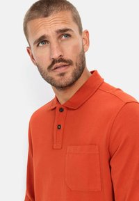Orange langærmet polo skjorte lavet af glat stof, med klassisk krave, tre-knaps lukning og en brystlomme med en syet detalje.