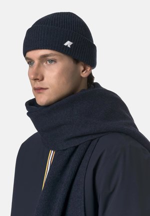 Cuffia a costine blu navy con logo e sciarpa coordinata. Entrambi gli articoli sono realizzati in tessuto a maglia lavorata, progettati per calore e comfort.
