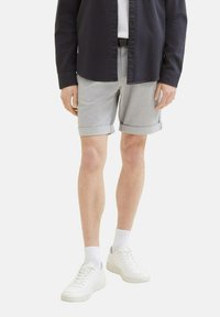 Pantalones cortos grises con puños enrollados en una tela ligera, combinados con una camisa oscura y zapatillas blancas, creando un atuendo casual.