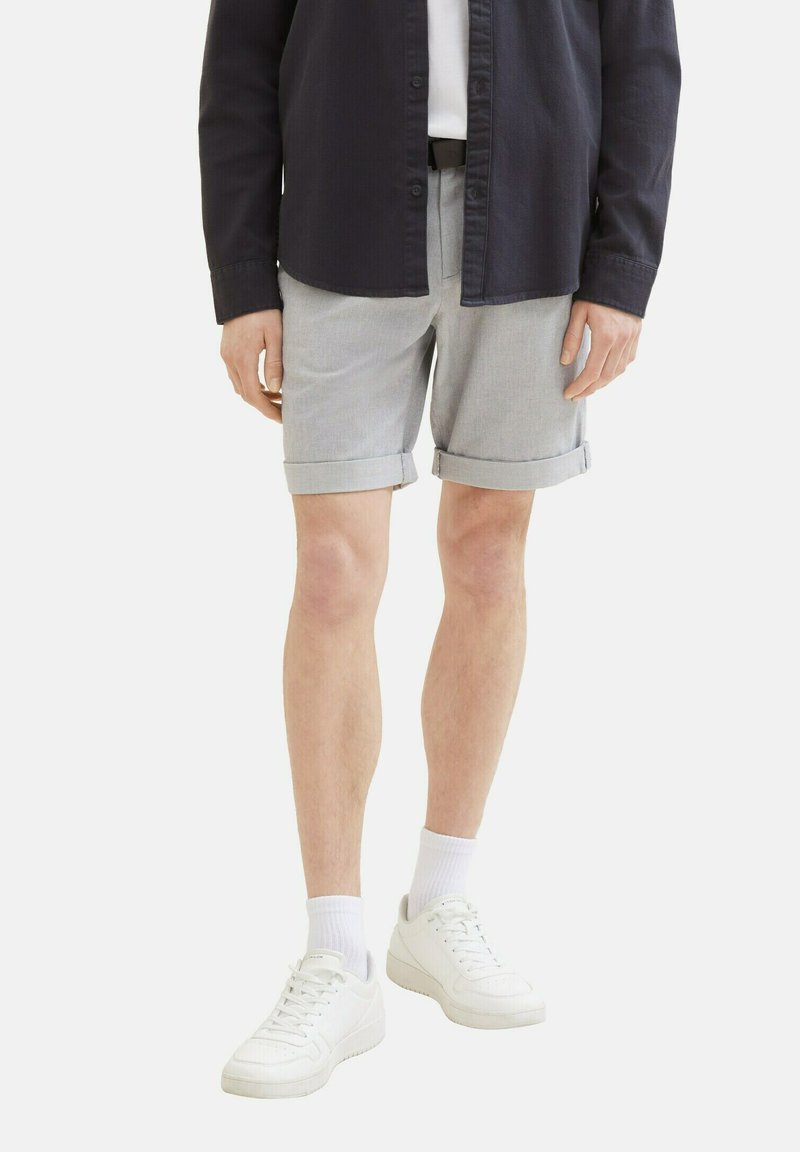 Pantalones cortos grises con puños enrollados en una tela ligera, combinados con una camisa oscura y zapatillas blancas, creando un atuendo casual.