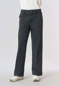 Pantaloni in cotone grigio scuro con design a gamba dritta, dotati di chiusura con bottone, due tasche laterali e una texture sottile. Abbinati a scarpe sportive bianche.