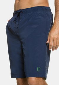 Marinefarbene Badeshorts mit elastischem Bund, verstellbarem Kordelzug und einem kleinen grünen Logo am unteren linken Bein. Glatte Textur, ohne Taschen.