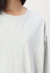 Světlé šedé mikina s dlouhým rukávem vyrobená z měkké bavlněné směsi, která má kulatý výstřih avolný střih s jemnou texturou.