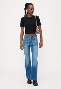 Melna ribota cropped t-kreklu, gaiši zilas flared denim bikses un melnas masīvas zābaki. Nelieli zebra svītraini rokassomiņa pāri plecam.