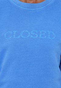 Sweat-shirt bleu avec le mot "CLOSED" brodé sur la poitrine en fil bleu assorti.