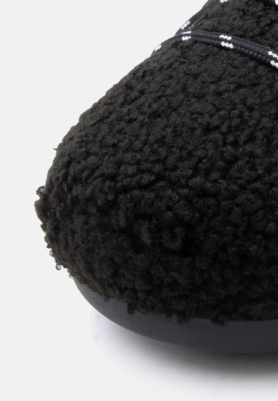 Chaussures noires duveteuses avec une surface texturée, une forme arrondie et une semelle noire lisse. Présentent un lacet contrasté à motif sur le dessus.