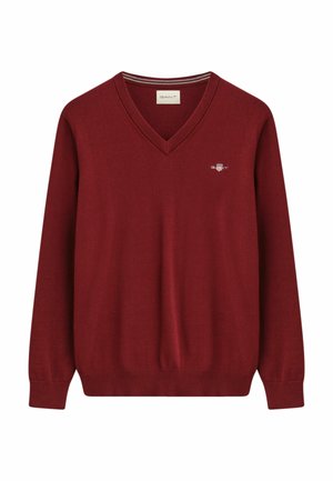 Pull en tricot rouge avec un col en V, des manches longues, des poignets et un ourlet côtelés, présentant un petit logo sur la poitrine et des détails rayés à l'intérieur du col.