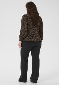 Dunkelbraunes Langarmoberteil mit einem Blumenmuster, gerafften Ärmeln und elastischen Bündchen, kombiniert mit schwarzen geraden Hosen.