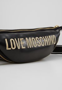Schwarze Leder-Gürteltasche mit goldgesticktem "LOVE MOSCHINO"-Logo, ausgestattet mit einem Reißverschluss und einem verstellbaren Gurt. Glatte Textur.