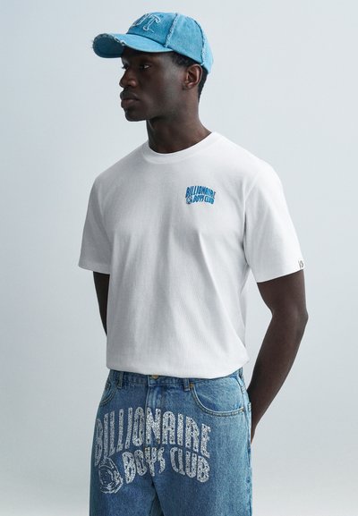 Λευκό βαμβακερό t-shirt με μπλε λογότυπο "Billionaire Boys Club" στο στήθος, σε συνδυασμό με ανοιχτόχρωμο μπλε τζιν παντελόνι με λευκά κείμενα γραφικών.