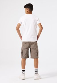 T-shirt blanc, shorts cargo beige avec poches latérales, baskets blanches et chaussettes à motifs noir et blanc, vues de l'arrière.