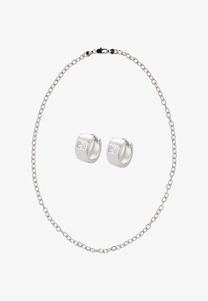 Ezüst lánc nyaklánc kapoccsal, két hozzáillő karika fülbevalóval, melyeket téglalap alakú átlátszó kövek díszítenek. Simított, fényes felületek.