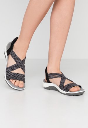 Black woven sandals with crisscross straps, a cushioned gray footbed, and a white and gray textured sole. Features an adjustable back strap.