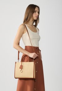 Woven straw handbag with brown faux leather accents, rectangular shape, short top handles, and a detachable shoulder strap.