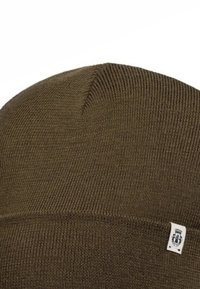 Brown ribbed knit beanie hat with a small white fabric tag featuring a black logo on the folded cuff.