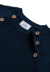 Marineblauer Strickpullover mit geripptem Kragen und Holzknöpfen an der Schulter. Mit einem Etikett, das "Stellav & Friends" zeigt. Glatte Textur.
