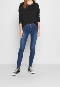 Jeans de mezclilla azul ajustados con una cintura de altura media, combinados con una camiseta de manga larga negra y zapatillas altas negras. Textura suave.