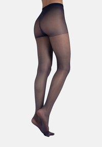 Weibliche Beine in transparenten schwarzen Strumpfhosen, von hinten gezeigt, mit einem leicht erhöhten Fuß vor einem schlichten weißen Hintergrund.