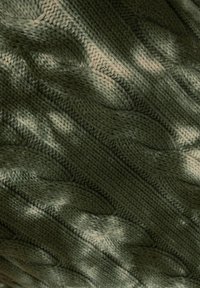 Ein strukturierter Stoff im Kabelstrickmuster in verschiedenen Grüntönen, der mit variierenden Schattierungen und subtilen Highlights Tiefe und Dimension schafft.