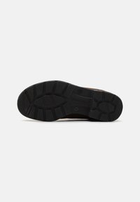 Suela de goma negra con un patrón de agarre texturizado. Diseño duradero y robusto con bordes redondeados y detalle del logotipo de la marca.