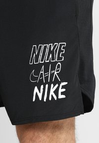 Short Nike noir avec texte stylisé blanc indiquant "NIKE AIR NIKE" et petit logo Nike Swoosh sur la cuisse gauche.