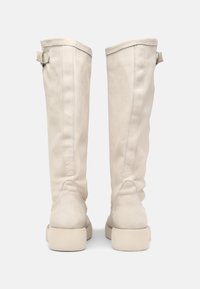 Botas de cuero blancas hasta la rodilla con una textura suave, que presentan un caña alta y estructurada y suelas planas y anchas. Detalle de pequeña hebilla en la parte superior.