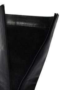 Bota de cuero negro con una textura suave, que presenta un cierre de cremallera a lo largo de un lado y un forro de tela oscura visible desde la abertura.